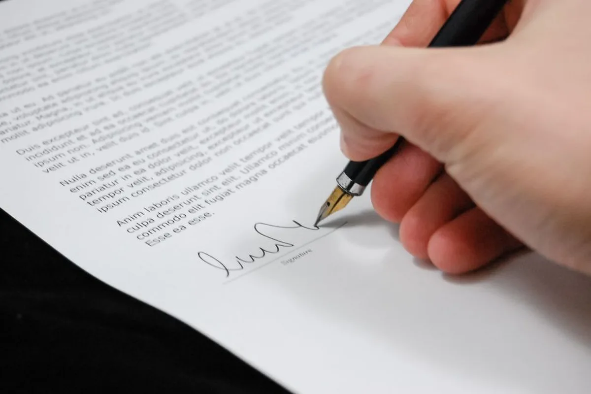 Une main signe un document officiel avec un stylo à plume.
