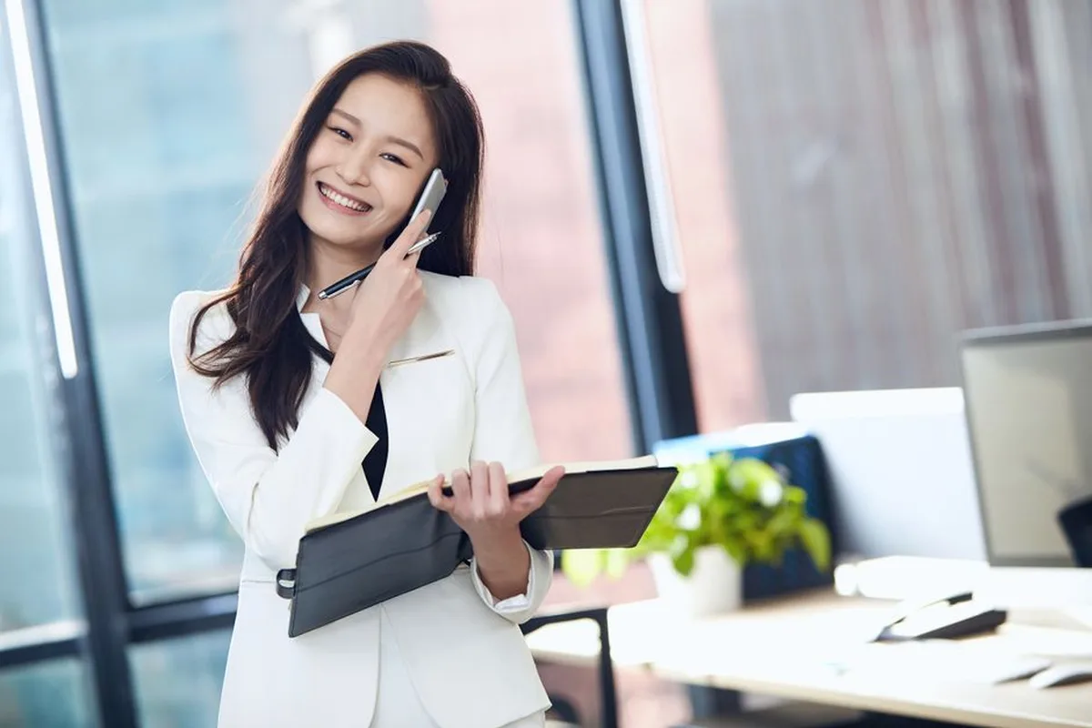 Une femme souriante prend un rendez-vous au téléphone tout en tenant son agenda.