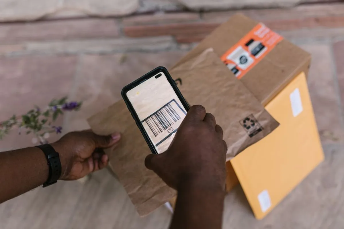 Une main scanne le code-barres d'un colis avec un smartphone.