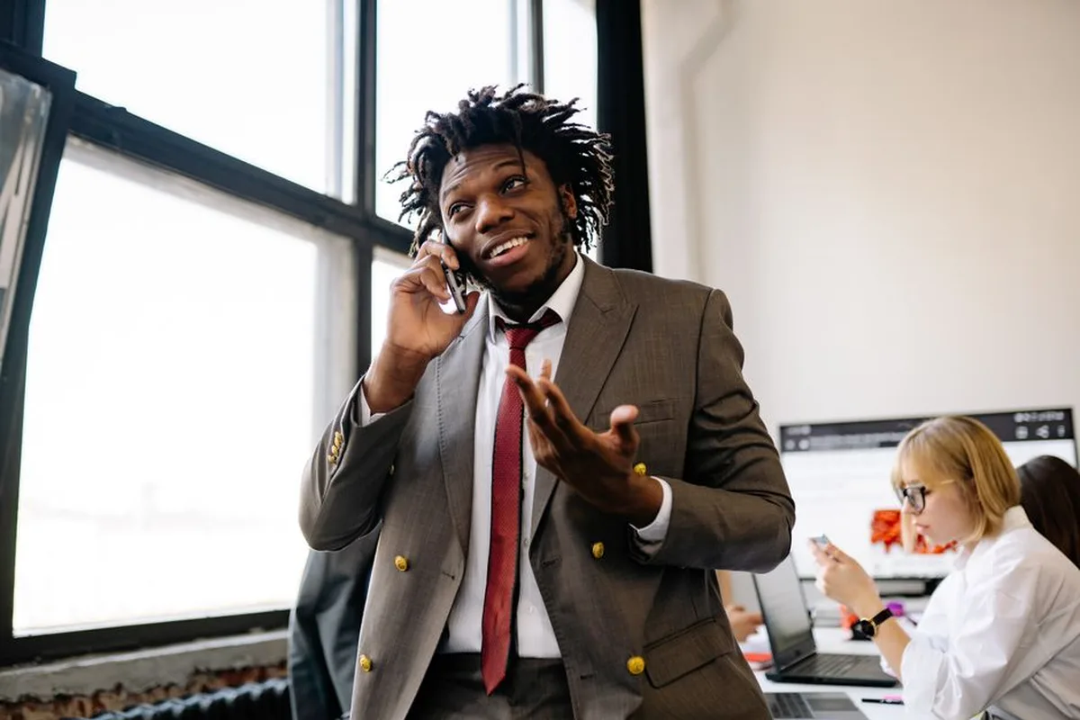 Un homme souriant en costume parle au téléphone dans un bureau lumineux.