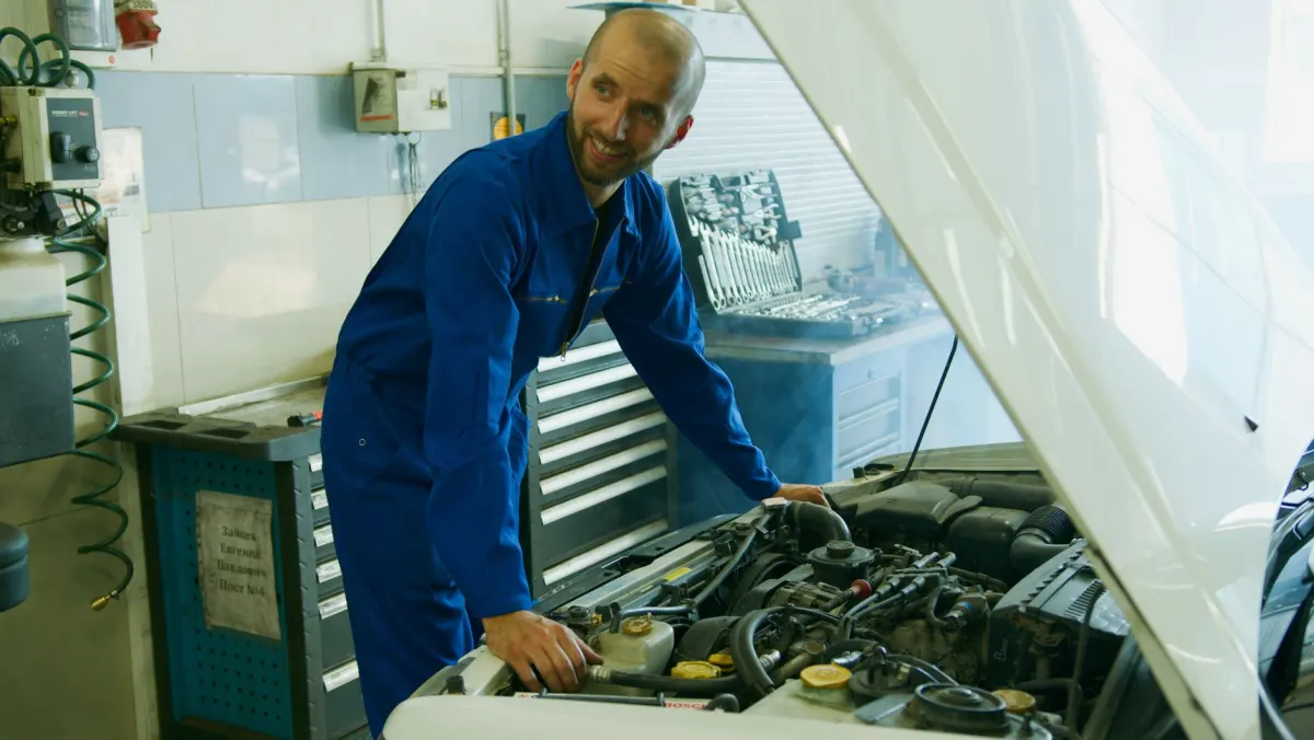 Mécanicien souriant réparant le moteur d'un véhicule en garage automobile