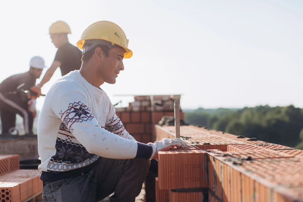 Maçon posant des briques sur un chantier ensoleillé, entouré de son équipe