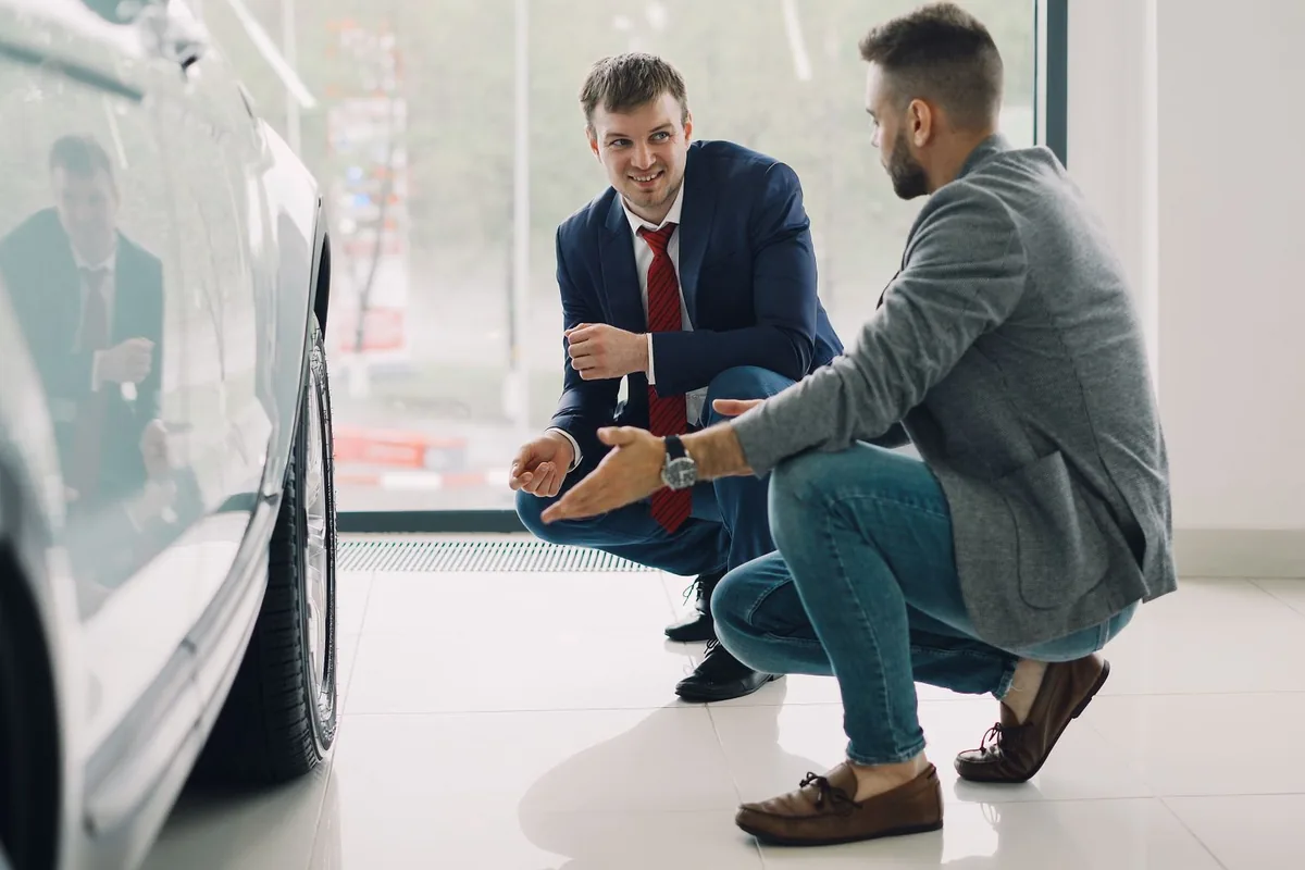 Vendeur automobile présentant un véhicule neuf à un client dans un showroom de concession
