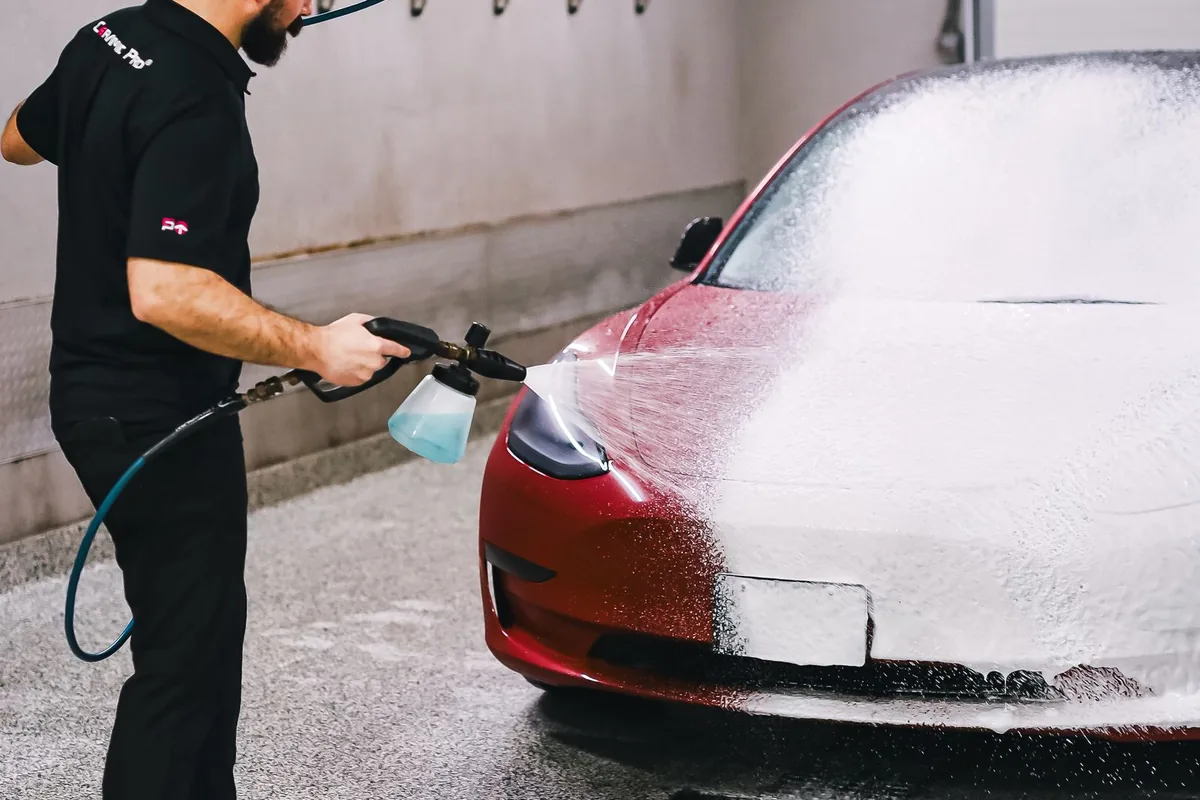 Employé appliquant une mousse nettoyante au canon à mousse sur une voiture en station de lavage
