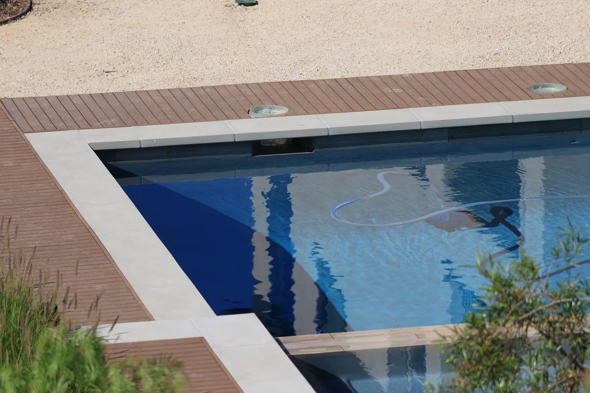 Piscine sereine à l'eau claire bordée d'une terrasse en bois, par une journée ensoleillée