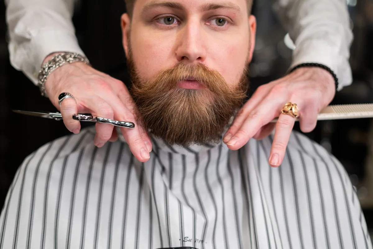 Barbier taillant la barbe d'un client dans son barbershop