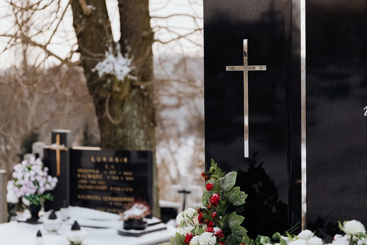 Pierre tombale en granit poli ornée d'une croix et de fleurs, sous la neige