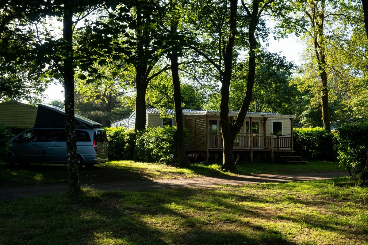 Mobil-home avec terrasse en bois sur un emplacement ombragé de camping