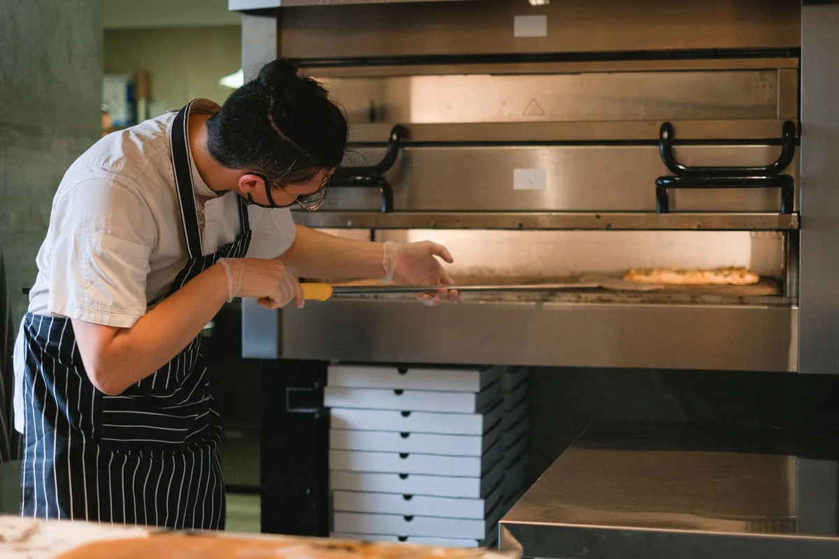 Pizzaiolo enfournant une pizza dans le four à bois d'une pizzeria