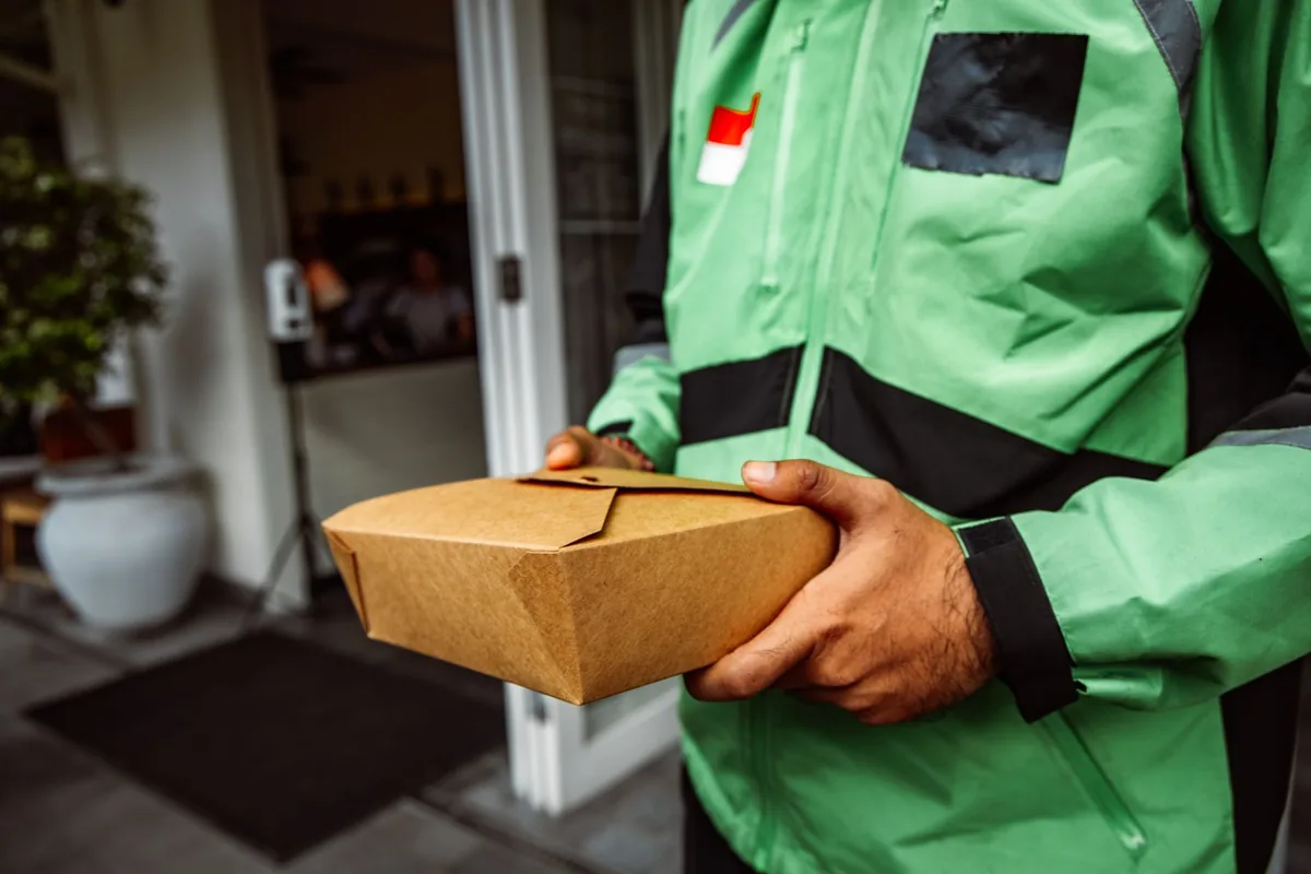 Livreur de repas remettant un plateau-repas à une personne âgée sur le pas de sa porte